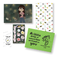 A collage of physical stationery and art designs, including an illustration of a character surrounded by fireflies, a patterned sheet, sticker sheet, a light bulb graphic sticker, and a green envelope card with text.